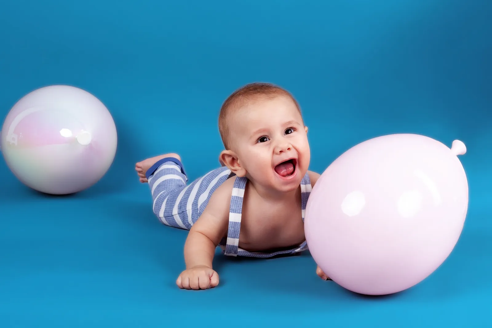 Lachendes Baby neben einem rosa Ballon vor blauem Hintergrund