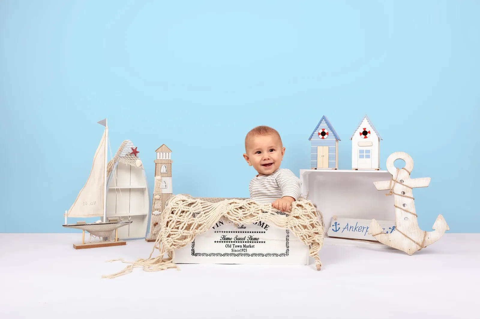 Lächelndes Baby in einem maritimen Studio-Set mit Segelboot, Leuchtturm und Anker