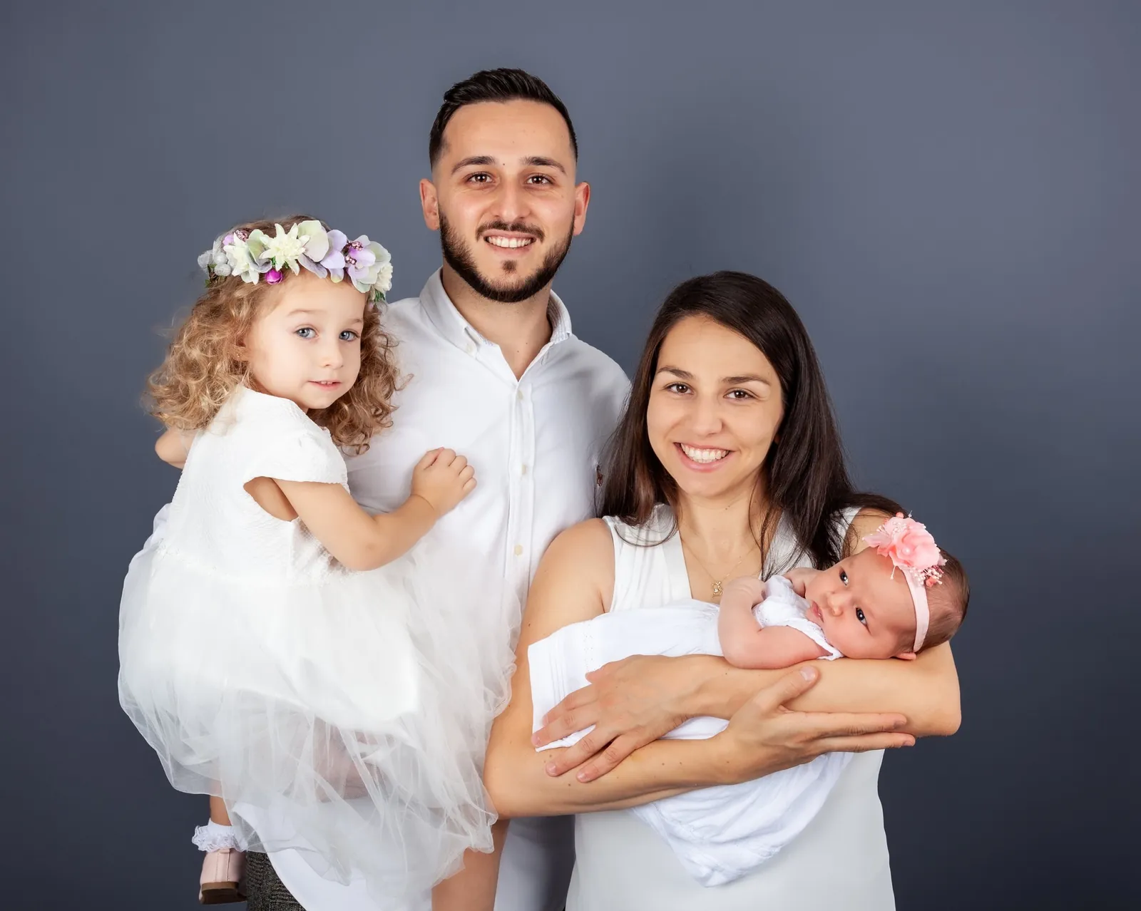 Familie in weisser Kleidung lächelt gemeinsam vor grauem Studiohintergrund