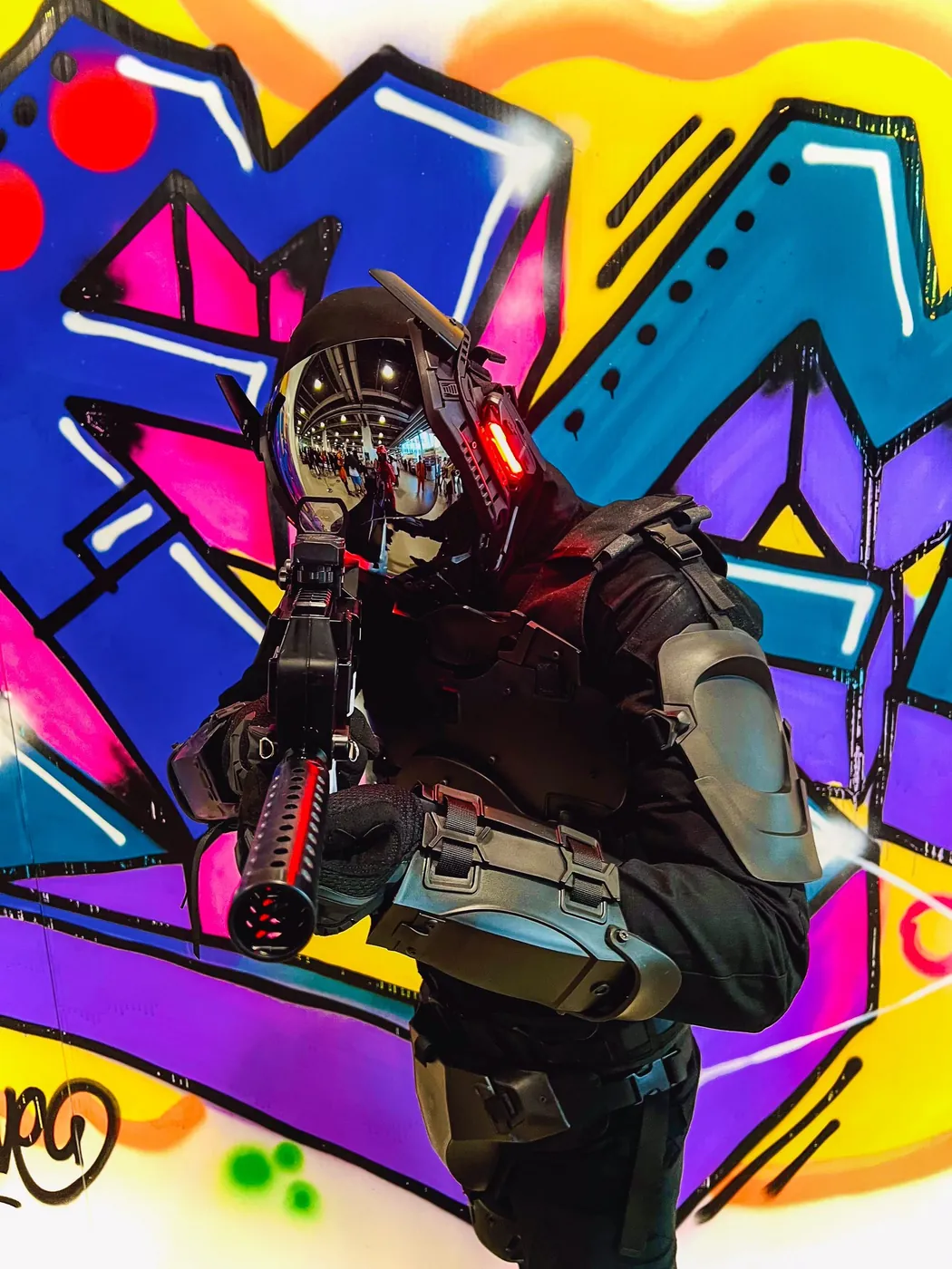 Cosplayer in taktischer Ausrüstung und verspiegeltem Helm vor farbigem Graffiti